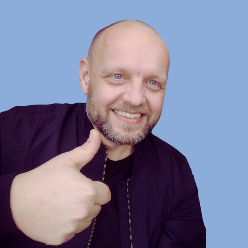 Ein Mann mit kahlköpfigem Haar und Bart zeigt Daumen hoch mit einem Lächeln vor einem blauen Hintergrund.