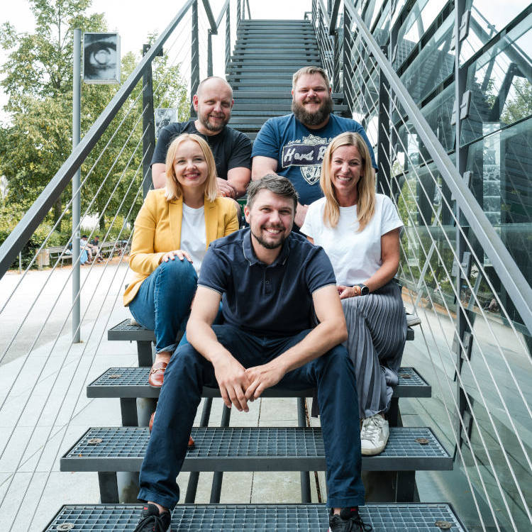 Vier Personen sitzen lächelnd auf einer Metalltreppe im Freien.